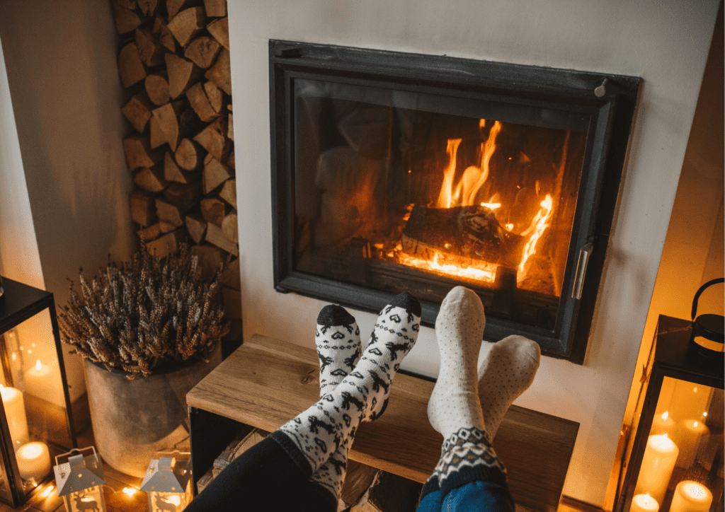 2 kişi ayaklarını şömineye karşı uzatmış huzurlu ve sıcak bir ortamda keyif yapıyor.